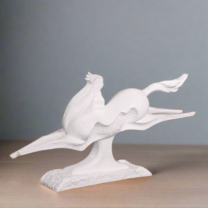 White ceramic sculpture of a bird on a branch with a blurred indoor background