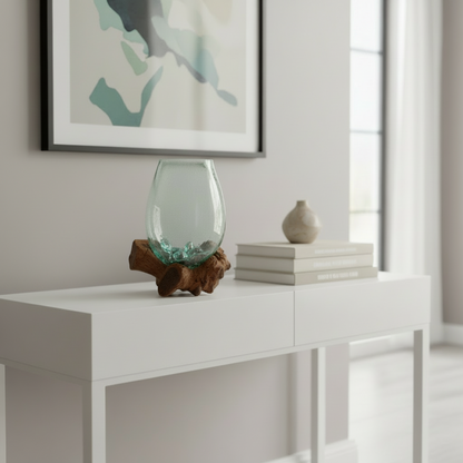 Glass vase with green plant on a wooden base against a blurred background