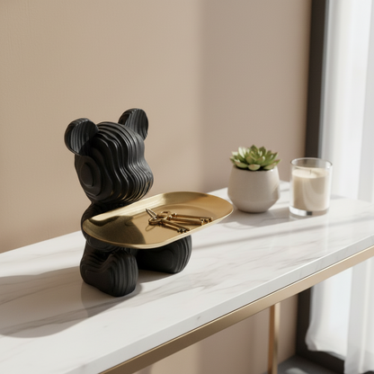Black bear-shaped object with a gold plate on a white surface