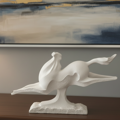 White ceramic sculpture of a bird on a wooden surface with a painting in the background