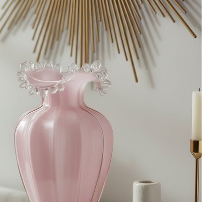 Pink vase with decorative top on a surface with books and flowers in the background