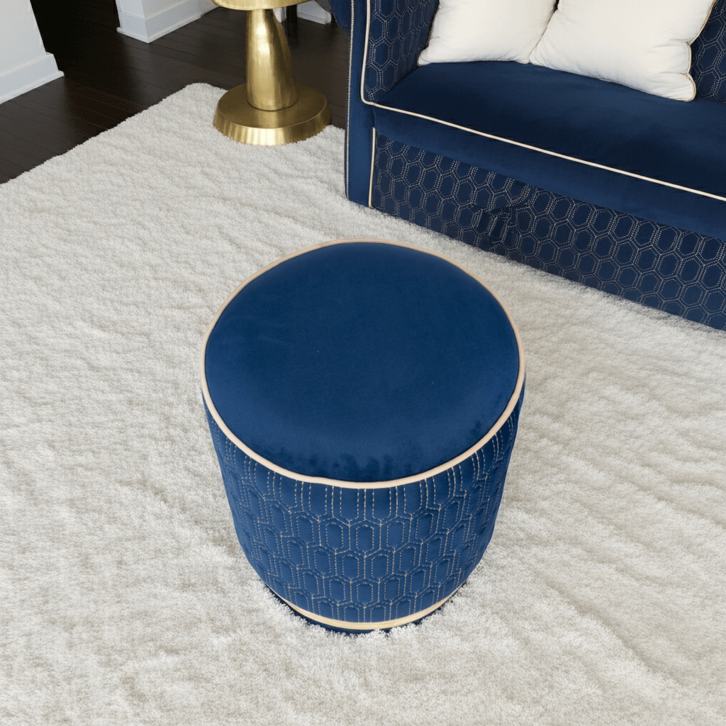 Geometric Stitched Velvet Ottoman in Navy on a plush rug with a sofa in the background.